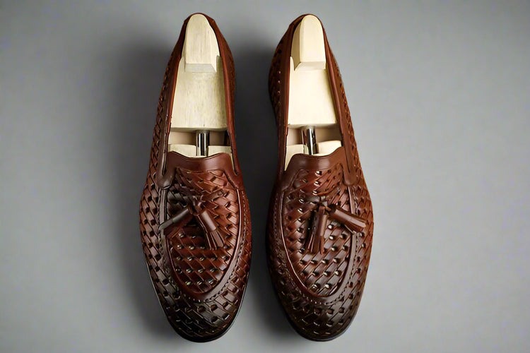 Pair of brown leather loafers with tassels on a wooden surface