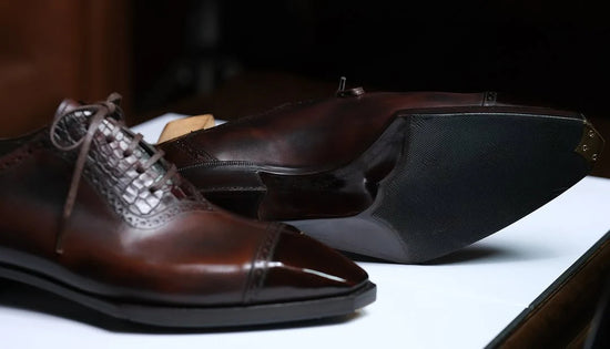 Brown leather dress shoes with silver accents on a white surface