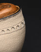 Close-up detail of a light beige textured leather shoe upper with decorative circular cutouts and a brown wooden shoe tree insert visible at the top against a dark background.