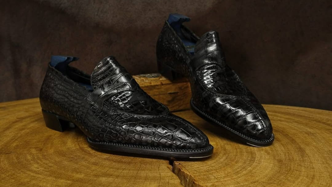 Black crocodile skin shoes on a wooden surface with a dark brown background