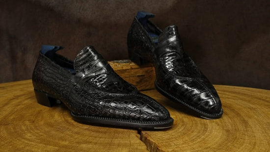 Black crocodile skin shoes on a wooden surface with a dark brown background