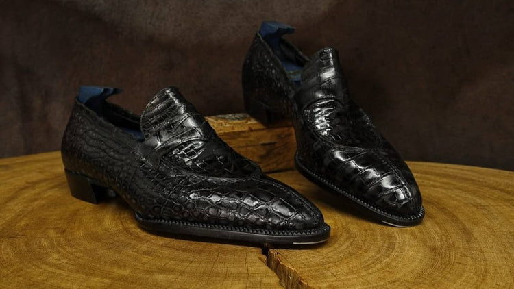 Black crocodile skin shoes on a wooden surface with a dark brown background