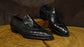 Black crocodile skin shoes on a wooden surface with a dark brown background