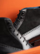 Close-up of a black suede and leather lace-up boot against a bright orange background.