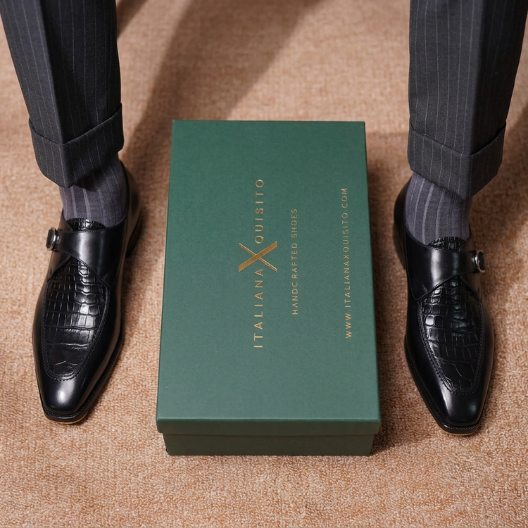 A pair of black embossed leather monk-style dress shoes worn with dark pinstriped trousers and gray socks, arranged symmetrically around a dark green box printed with the brand name 'ITALIANO LOUISITO'.
