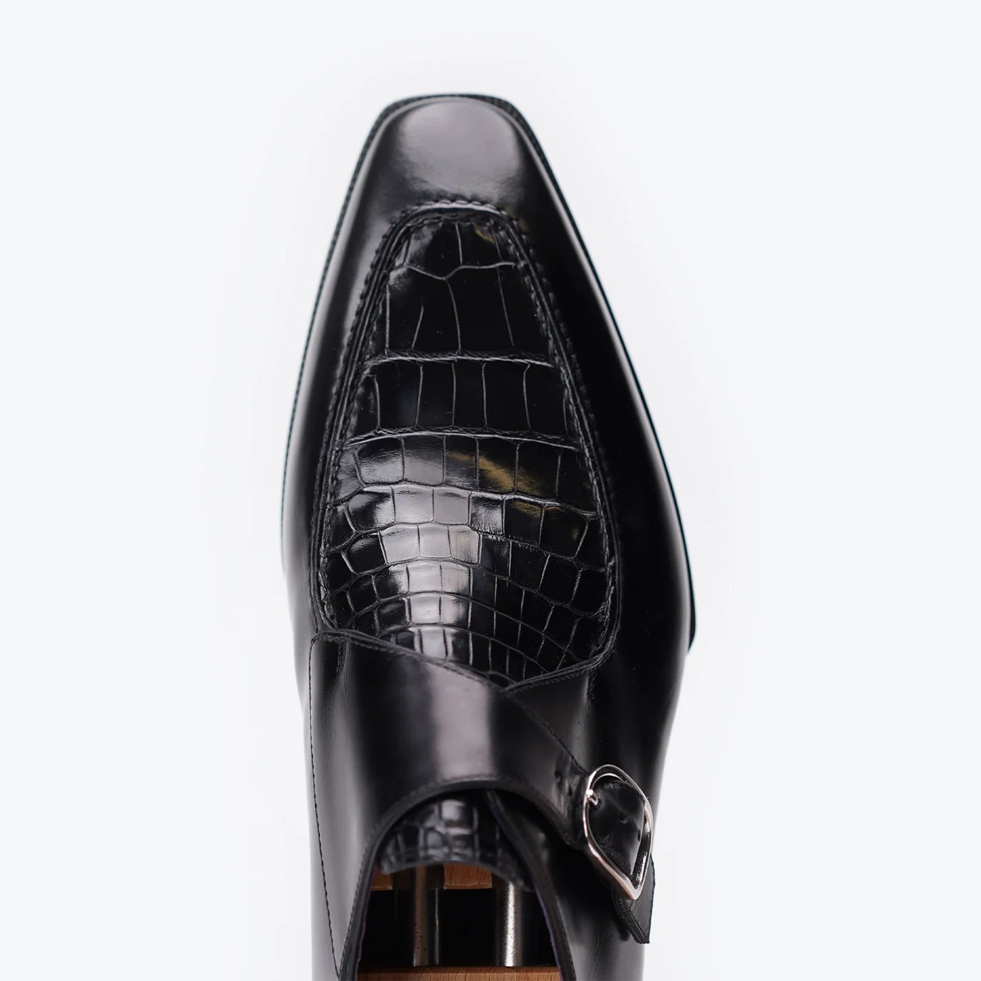 A close-up top-down view of a black leather dress shoe with a crocodile-embossed panel on the vamp and a silver buckle strap, set against a plain white background.