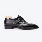 A black double monk strap leather shoe with a toe cap featuring a crocodile-embossed pattern, displayed on a light wood shoe tree against a clean white background.