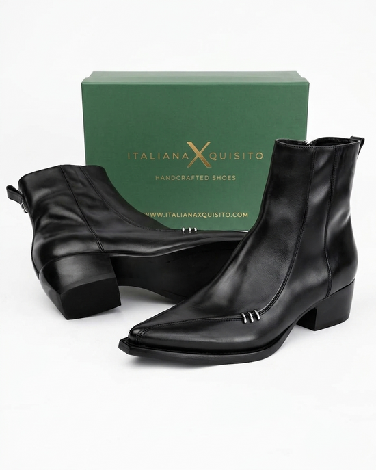 A pair of black leather ankle boots with low block heels and silver decorative studs, displayed in front of a green Italian X Quisito brand box on a white background.