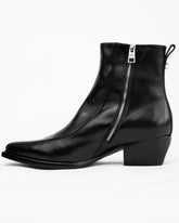 A black leather ankle boot with a side zipper, low block heel, and pull tab, shown from a side profile on a white background.