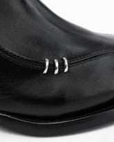Close-up of a black leather boot featuring three polished silver metal decorative rings on the side, set against a plain white background.