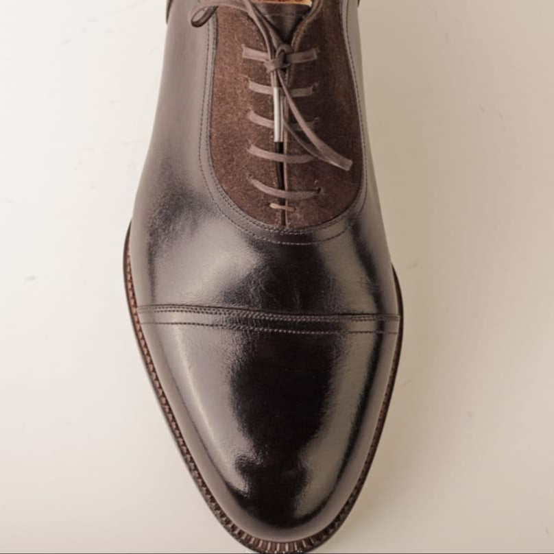 Shiny brown leather dress shoe on a light beige background