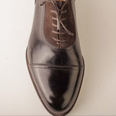Shiny brown leather dress shoe on a light beige background
