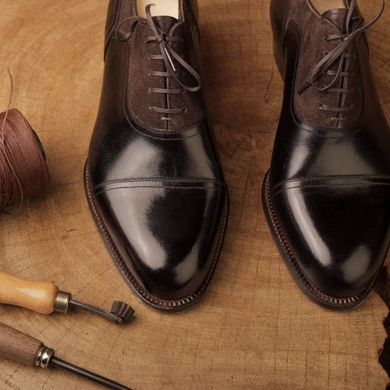Pair of polished brown dress shoes on a textured brown surface with shoe tools.
