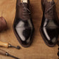 Pair of polished brown dress shoes on a textured brown surface with shoe tools.