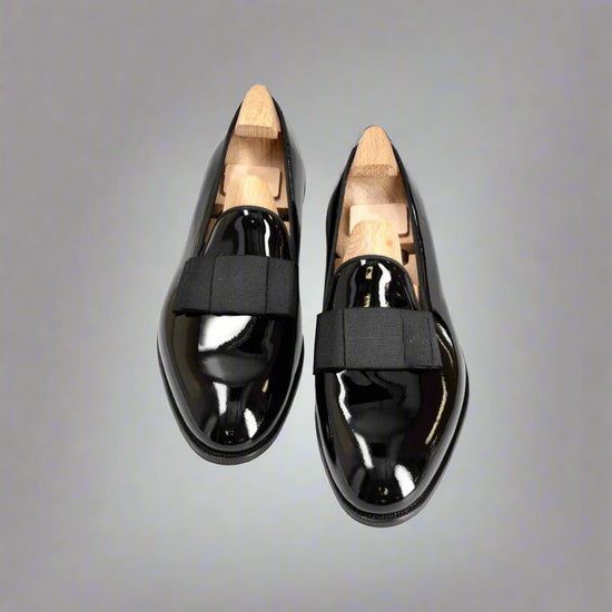 Pair of black patent leather shoes with wooden soles on a white background