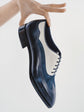 A hand holds a navy blue and white leather wingtip oxford shoe against a clean white background.