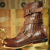 A brown embossed leather ankle boot with multiple buckle straps, shown standing on its beige sole against a rustic wooden background.