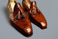 Brown leather loafers with tassels on a wooden surface