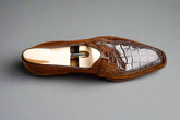 Brown leather loafer with white crocodile-patterned insole on a wooden surface