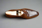 Brown leather loafer with white crocodile-patterned insole on a wooden surface