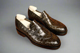Pair of brown crocodile skin loafers on a wooden surface