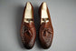 Pair of brown leather loafers with tassels on a wooden surface