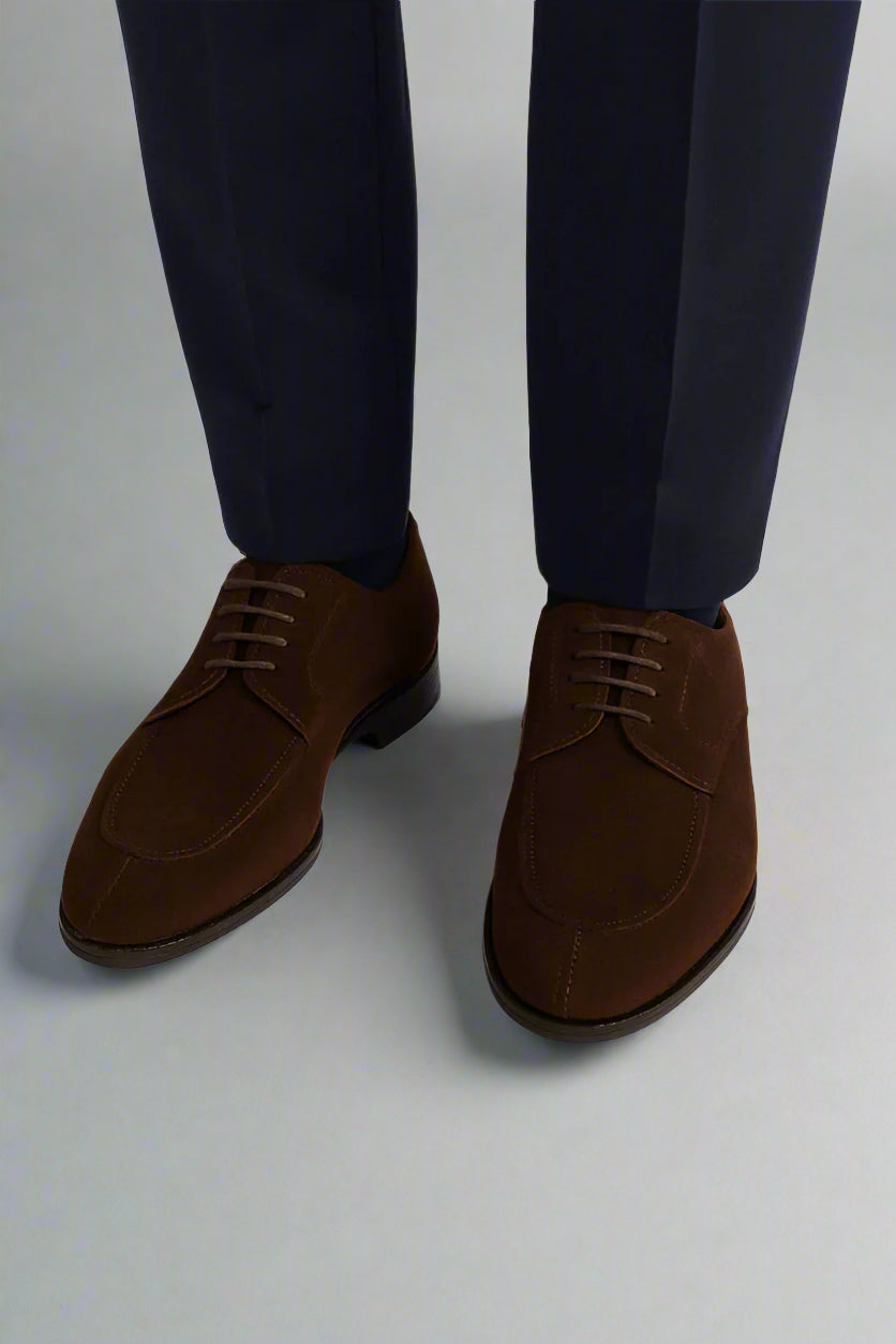 Brown suede shoes worn with navy pants on a white background