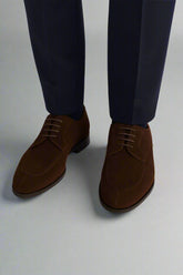 Brown suede shoes worn with navy pants on a white background