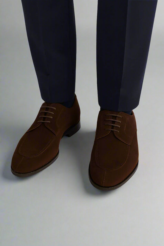 Brown suede shoes worn with navy pants on a white background