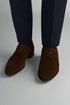 Brown suede shoes worn with navy pants on a white background