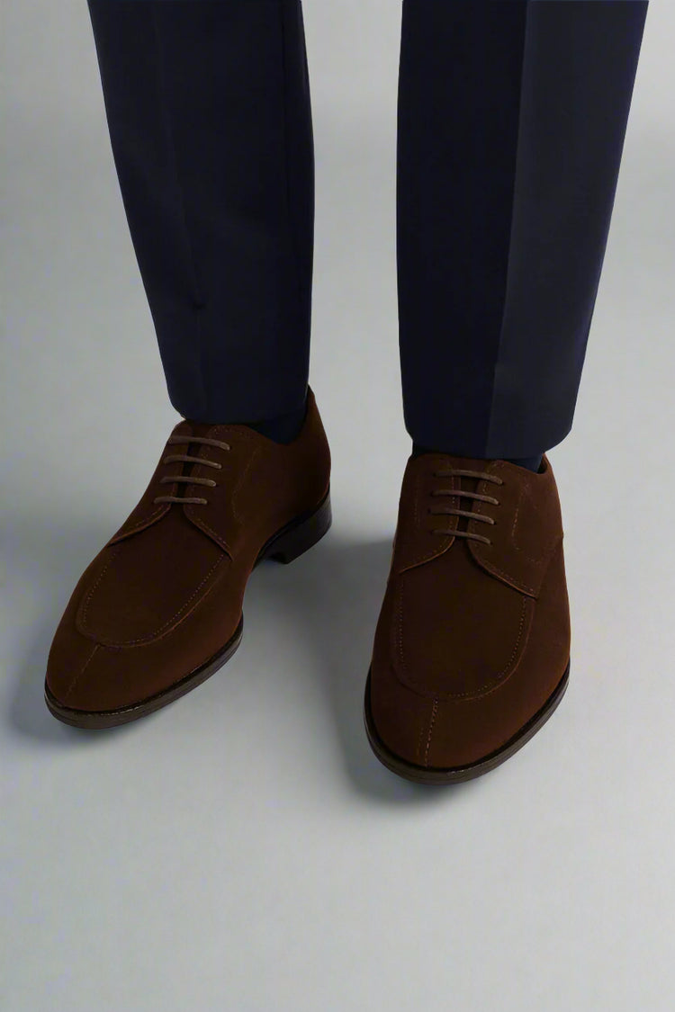 Brown suede shoes worn with navy pants on a white background