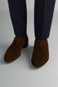 Brown suede shoes worn with navy pants on a white background