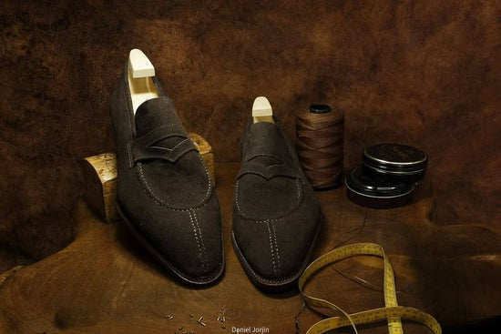 Pair of brown loafers on a textured brown surface with spools of thread and a measuring tape.