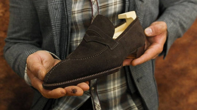 Person holding a brown loafer shoe with a wooden insole against a blurred background