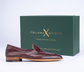 A single burgundy leather loafer shoe with a stacked wooden heel, positioned in front of its dark green branded shoebox on a white background.