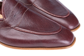 A close-up of a pair of men's penny loafers in dark burgundy pebbled leather, showing the toe, vamp, and side stitching against a white background.