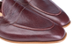 A close-up of a pair of men's penny loafers in dark burgundy pebbled leather, showing the toe, vamp, and side stitching against a white background.