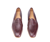 A pair of burgundy leather penny loafers with a pointed toe, shown from a top-down view on a white background.