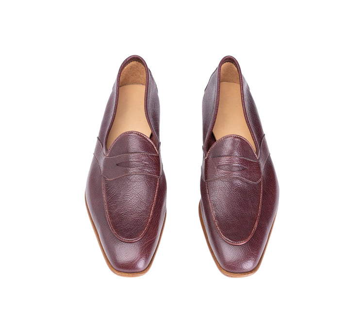 A pair of burgundy leather penny loafers with a pointed toe, shown from a top-down view on a white background.