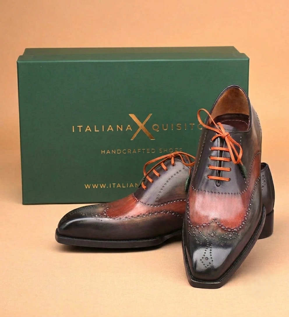 A pair of men's wingtip oxford shoes with a dark brown and reddish-brown brogue design, orange laces, and a dark green branded shoebox behind them on a beige background.