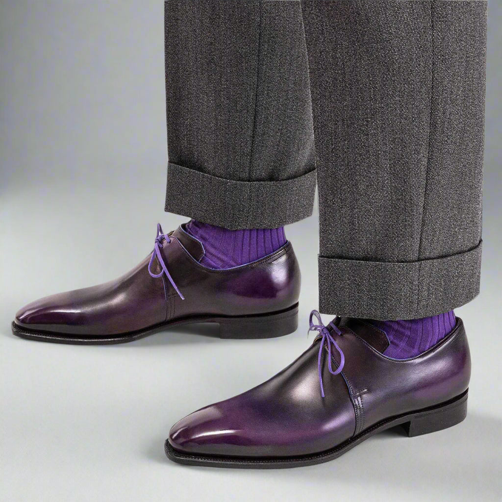 Purple dress shoes with gray trousers and purple socks on a white background