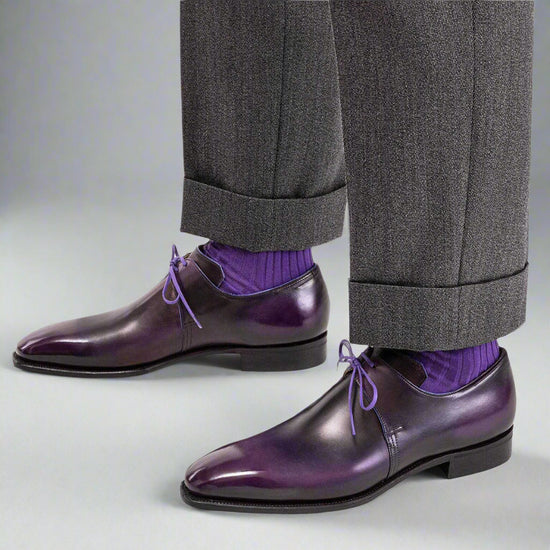 Purple dress shoes with gray trousers and purple socks on a white background