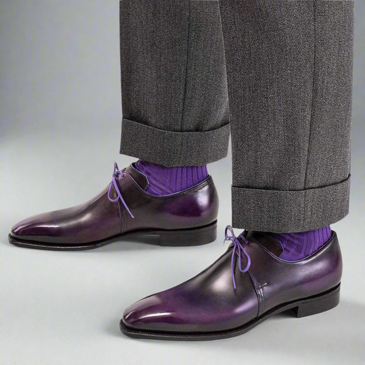 Purple dress shoes with gray trousers and purple socks on a white background