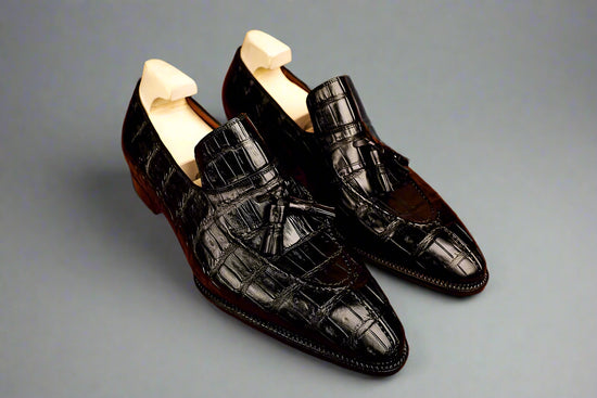 Pair of black crocodile skin shoes on a wooden surface