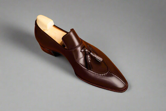 Brown leather loafer with tassels on a wooden surface