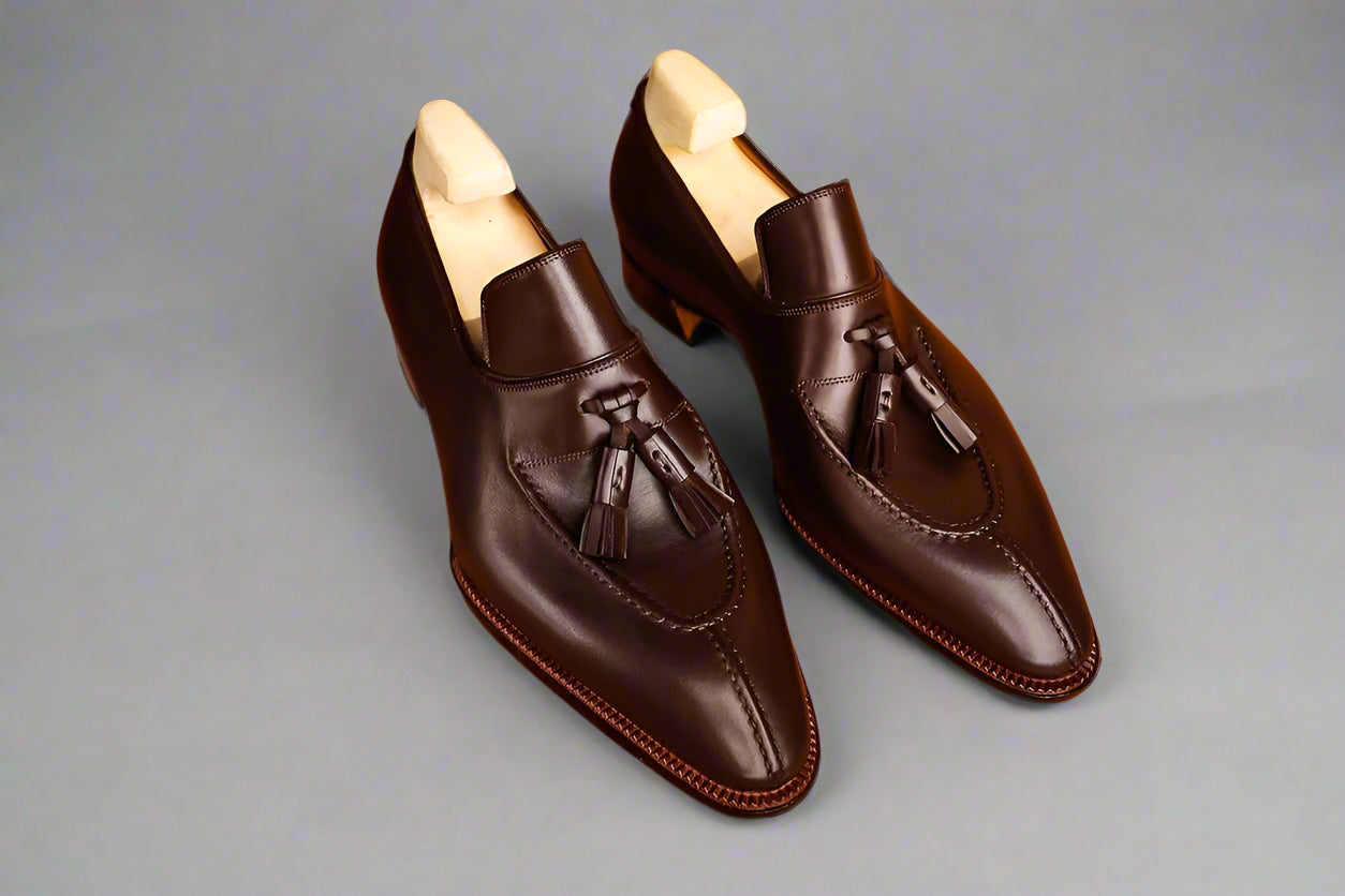 Pair of brown leather loafers with tassels on a wooden surface