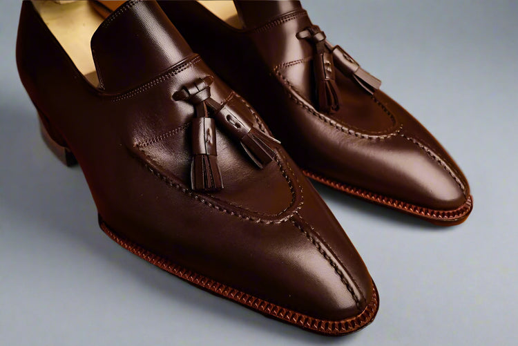 Pair of brown leather loafers with tassels on a wooden surface