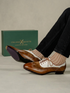 A person wearing brown and white wingtip oxford shoes with striped socks, with the green Italian X Quisito shoebox in the background.