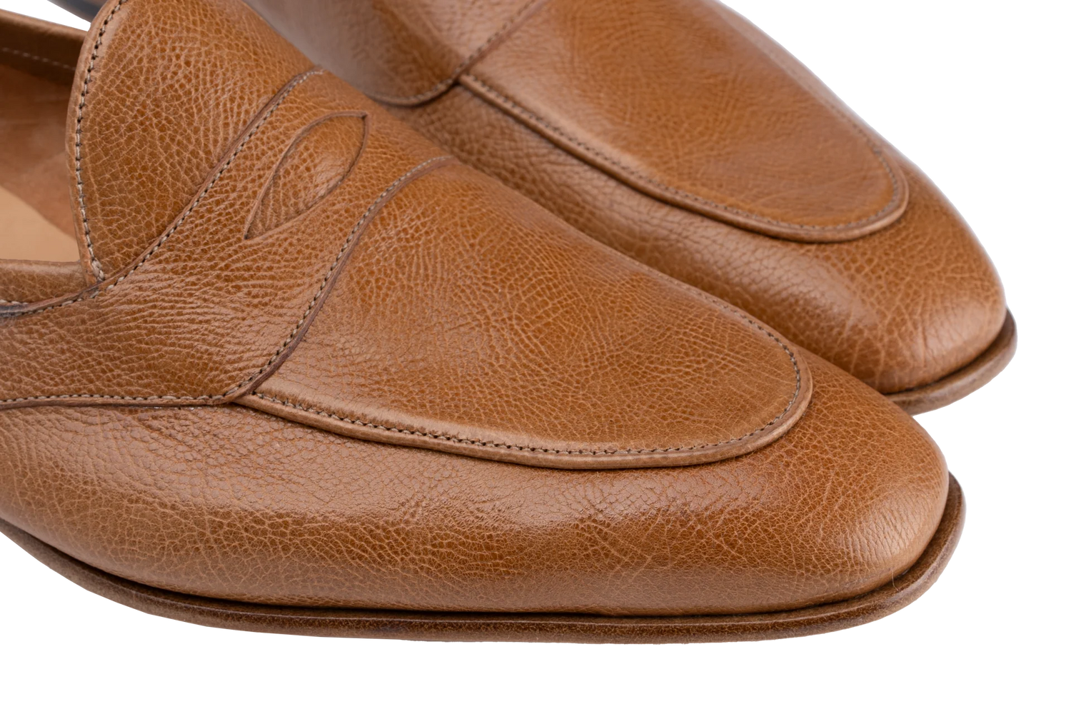 Close-up of a pair of tan leather penny loafers with a pebbled texture, showing the toe and side panels against a white background.