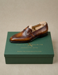 A single brown leather loafer shoe with a tan insole, displayed on top of a dark green shoebox with the brand name 'Italianxquisito' printed in gold.